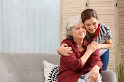 Elderly woman with female caregiver in living room.