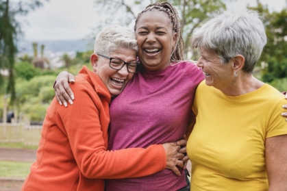 Three senior women laughing and hugging outdoors, celebrating friendship and strong community connections in senior living.