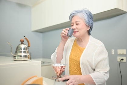 A senior woman enjoys the aroma of coffee in a kitchen, illustrating the connection between scent and memory.