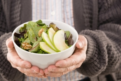 An older adult holding a MIND diet-inspired salad featuring leafy green vegetables and nuts.
