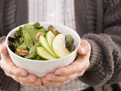 An older adult holding a MIND diet-inspired salad featuring leafy green vegetables and nuts.