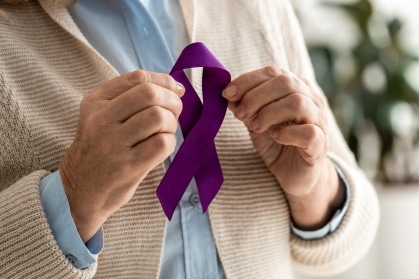 Senior holding a purple Alzheimer's awareness ribbon in support of memory care and advocacy