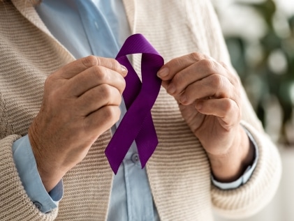 Senior holding a purple Alzheimer's awareness ribbon in support of memory care and advocacy