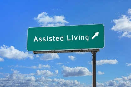 Green highway sign reading "Assisted Living" with an arrow pointing up and ahead against a blue sky, a symbol of deciding when it's time for assisted living
